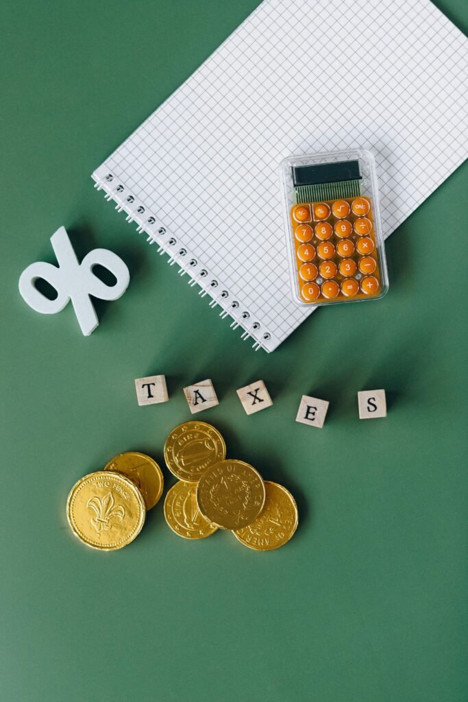 Flat lay of calculator, gold coins, notebook, and tax symbols on a green background.